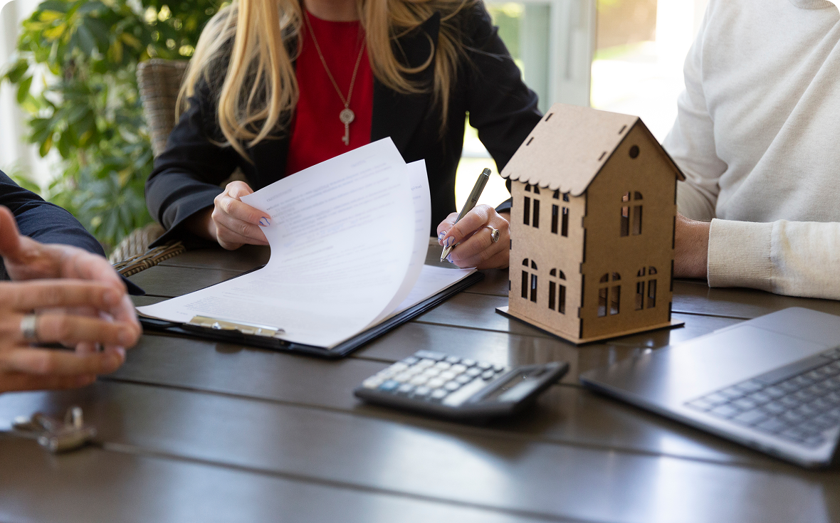 People signing documents near small house model.